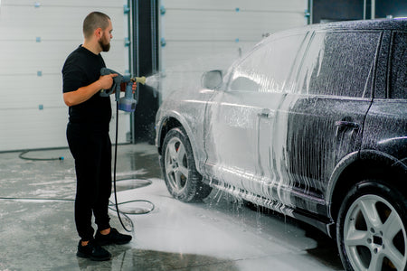 Professional car wash applying thick white foam to a black SUV with a foam spray gun — illustrative use of AutoBrite Purple Powder