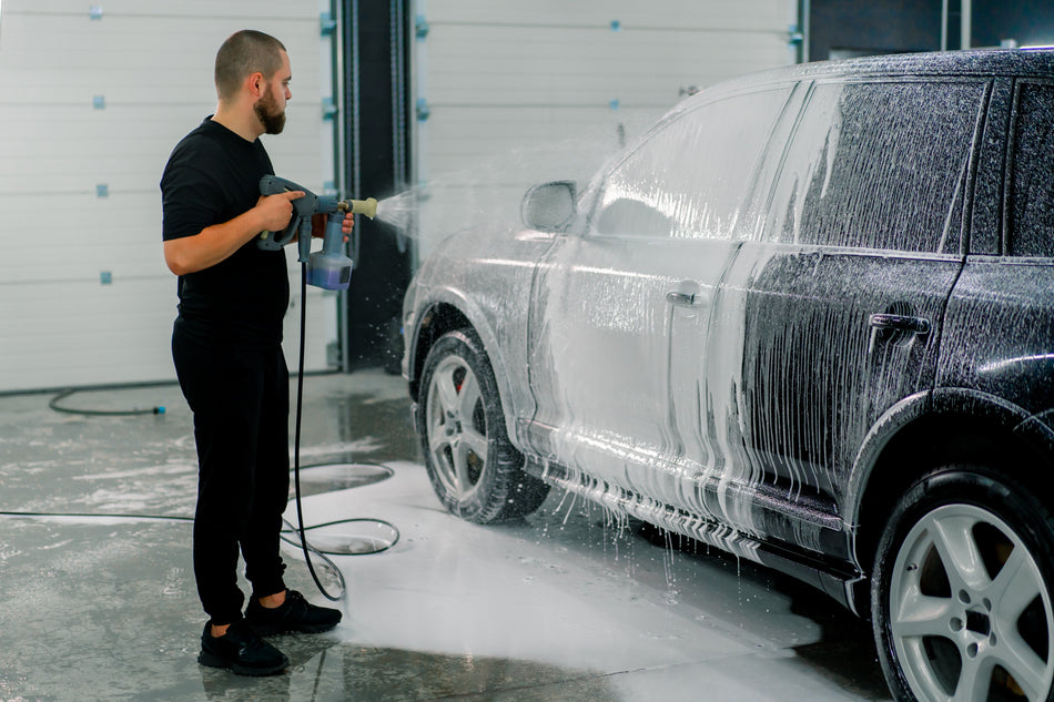 Professional car wash applying thick white foam to a black SUV with a foam spray gun — illustrative use of AutoBrite Purple Powder